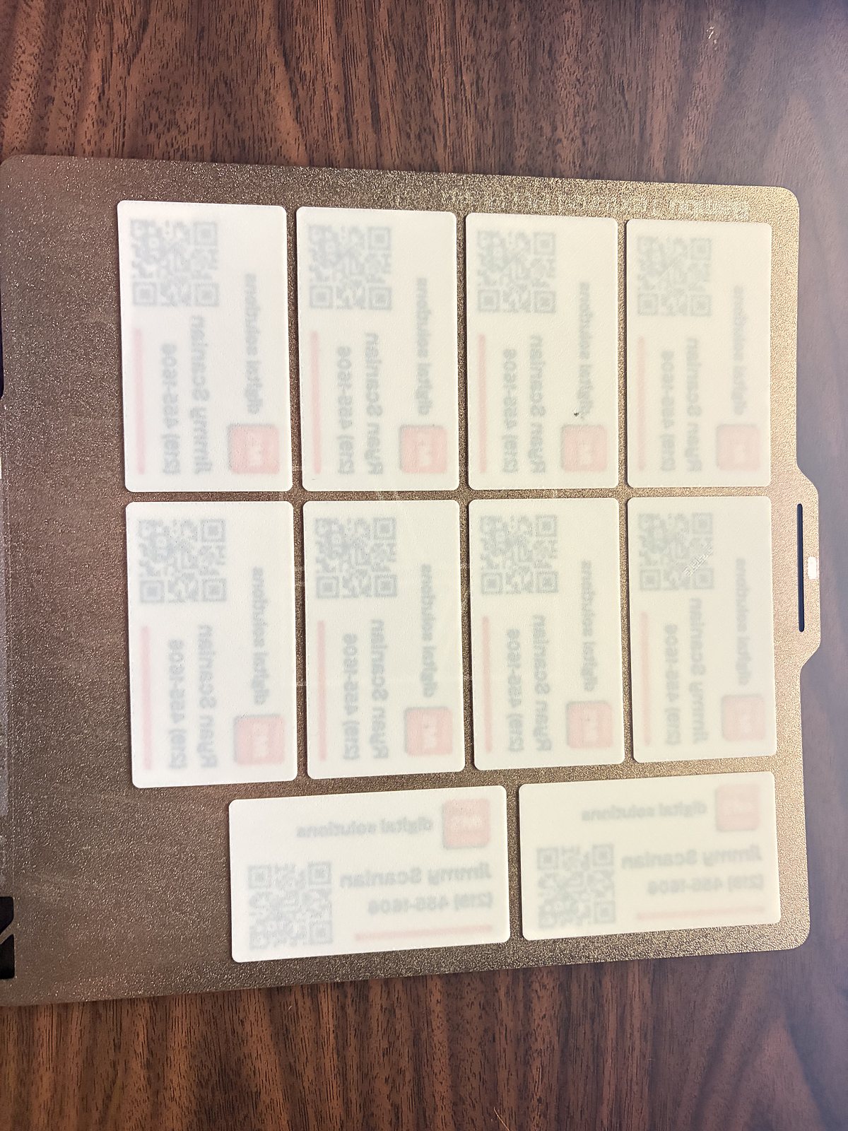 Ten finished cards laid out on the 3D printer's build plate, printed face down so every card takes the same matte texture from the plate