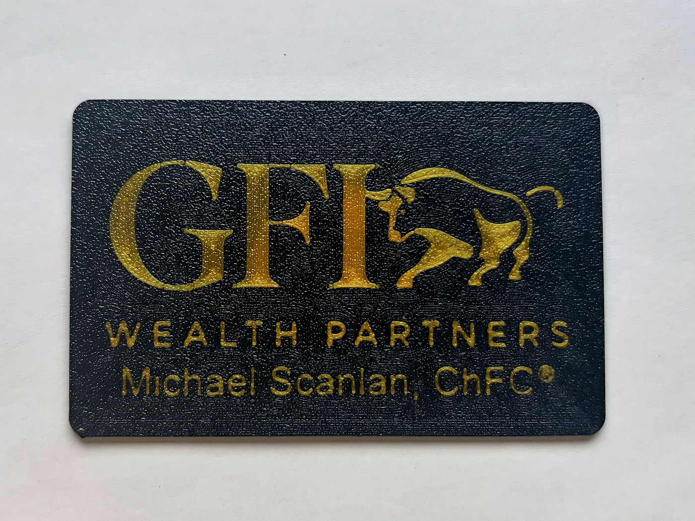 A matte black printed card for GFI Wealth Partners, the company name and a charging bull rendered in gold above the adviser's name