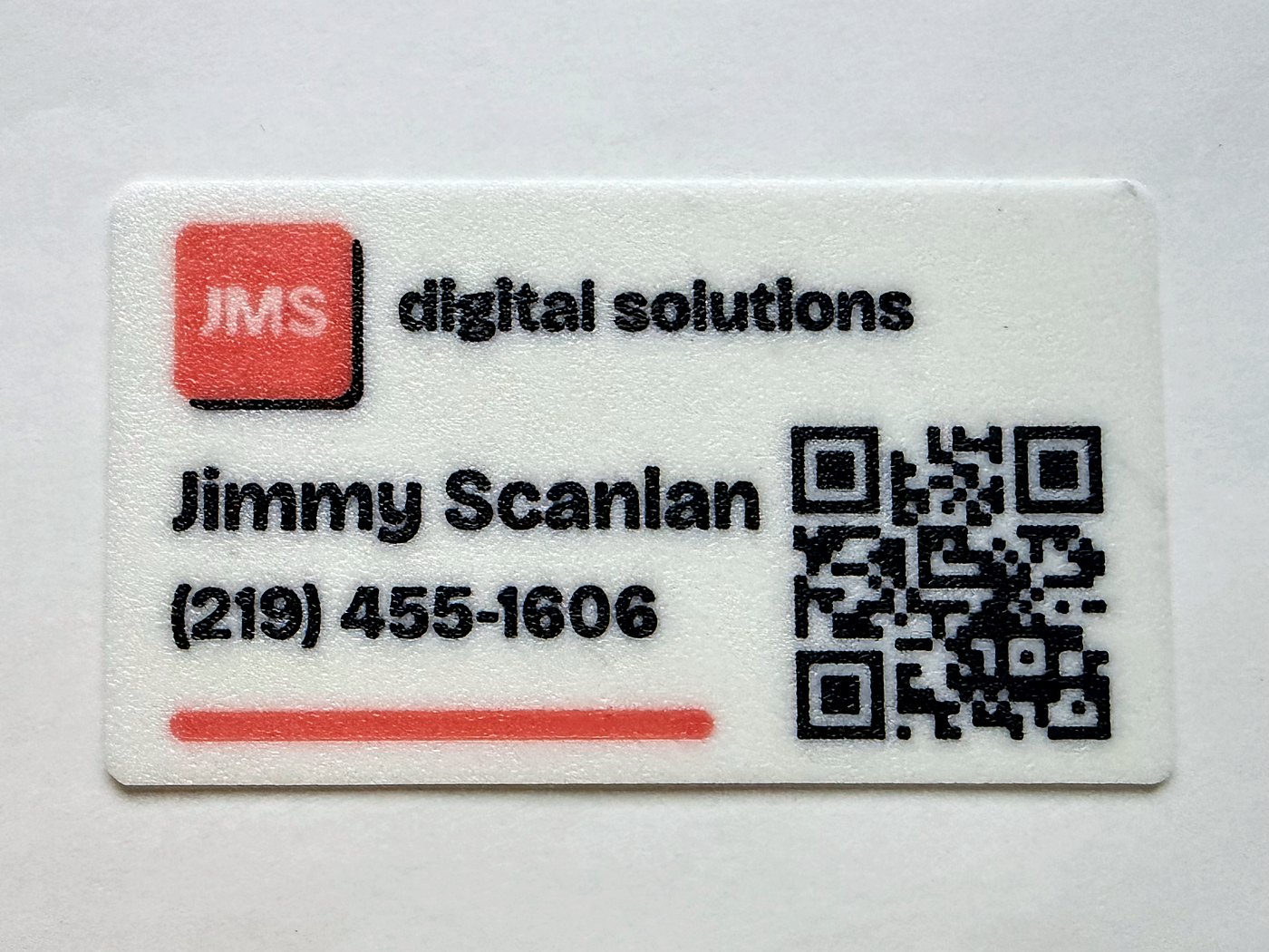 A white printed card for JMS Digital Solutions, with a coral logo tile, name, phone number and a printed QR code in black