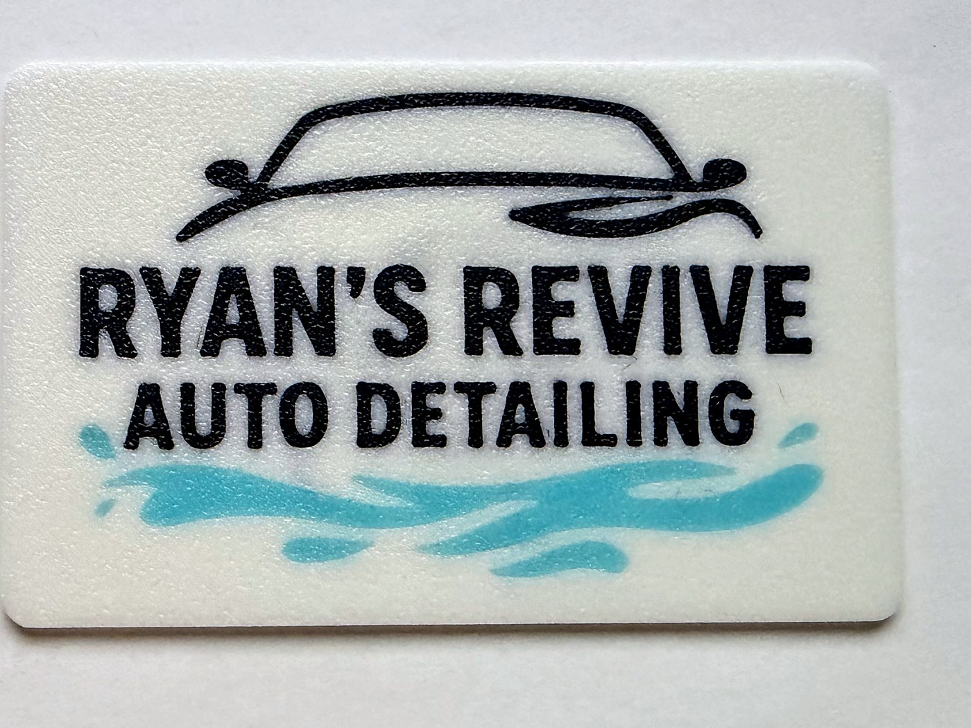 A white printed card for Ryan's Revive Auto Detailing, showing a car outline in black above the business name with a teal water splash beneath it